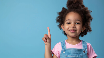 young African American girl with a big smile, wearing a pink shirt and a blue denim jumper, set against a light blue background