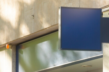 Blue sign mockup, somewhat aged and dirty, with copy space to put the logo, hanging from a facade, exterior, day