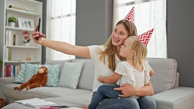 Caucasian mother and daughter making heartwarming birthday memories, hugging and taking a captivating self-picture together with a smartphone, from their cozy living room sofa.