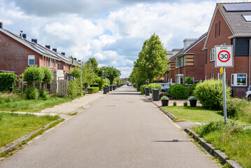 Street lined with brick houses in a suburban residential district on a cloudy summer day. Wheelie...