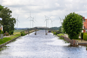 Wooden footbridge over a canal with a wind farm in background on a cloudy summer day