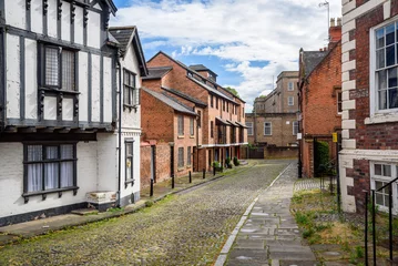Deurstickers Empty cobbled street lined with brick houses in a city centre on a partly cloudy summer day © alpegor