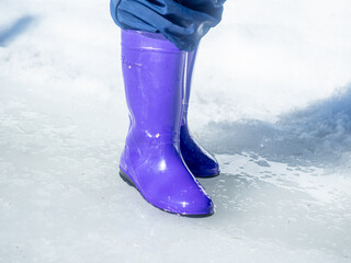 a child jumps in a puddle, in rubber boots, snow, puddle, winter, sunny, spring, thaw