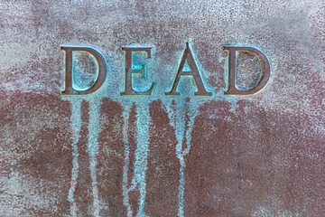 DEAD: Lettering DEAD on a bronze plate. Close-up of word DEAD on a bronze slab with oxidized green...