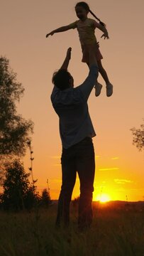Dad plays with his daughter, throws up child with his hands in sky, outdoors. Family game concept. Child, superhero, fly. Happy Father, child, little girl have fun together in park against sun. Kid