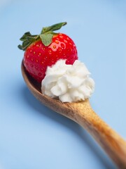 Strawberry and whipped cream on wooden spoon.