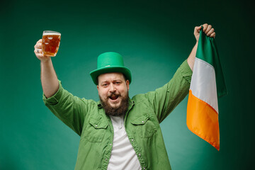 Happy bearded man with glass of beer and Irish flag on dark green background. St. Patrick's Day.