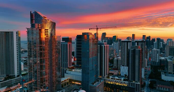 Drone approaching the high-rise buildings covered with light of setting sun. Amazing colorful sky at backdrop.
