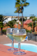 Glasses of cold white wine on roof terrace served outdoor in Corralejo, Fuerteventura in sunny day, pool with blue water