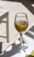 Glass of cold white wine on white terrace table outdoor in sunny day