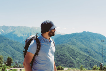 Naklejka premium millenial bearded tourist man wearing bucket hat, with backpack trekking in mountains