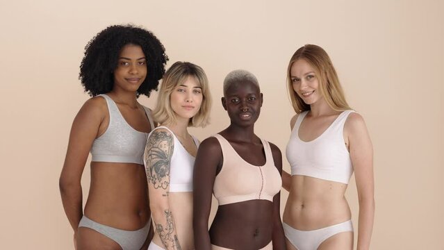 4 happy diverse women, four smiling gen z multiracial young girls friends beauty models group wearing underwear bonding looking at camera standing isolated on beige background, portrait.