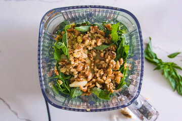 Healthy fresh meal cooking, nuts, greens in a blender, food preparation. Homemade vegetables for menu, advert or package, close up, selective focus.