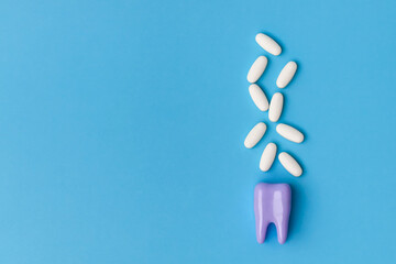 Dental care concept. Toothache pills. Purple tooth model and medical tablets on a blue background with copy space. Close up view of white pills and tooth model on blue background.