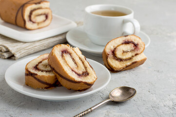 Roll with berry jam and chocolate whole and cut with a cup of tea on a light background. Horizontal, free space.