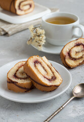 Roll with berry jam and chocolate whole and cut with a cup of tea on a light background. Close, free space.