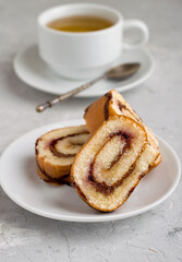 Roll with berry jam and chocolate in a cut with a cup of tea on a light background.