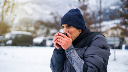 Hispanic handsome young man holding hot coffee or tea in snowy lanscape