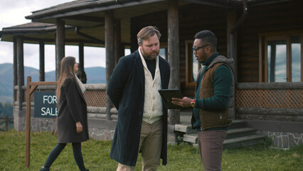 Fototapeta premium Family with kids visit potential home property. African American real state agent consults Caucasian man and shows plan of modern house on digital tablet computer. Residential property on sale concept