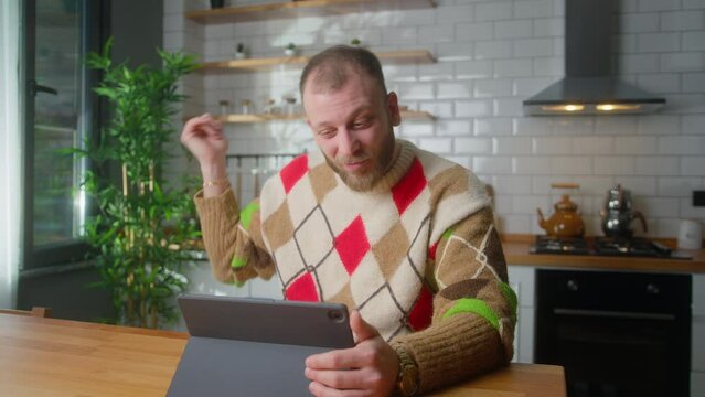 Smiling adult man sitting in the kitchen having video call conversation through tablet computer. Share news, talk to family, enjoy webchat virtual meeting