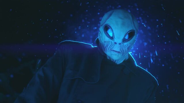 Alien from outer space standing under blinking ufo light and looking at camera outdoors on a snowy night. Low angle view