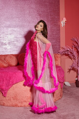 glamorous and young woman in pink feathered robe and gloves posing in a luxurious setting