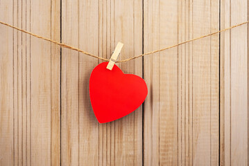 Red paper heart hanging on clothespins on wooden background. Love concept