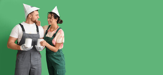 Happy young couple with paint cans on green background. Banner for design