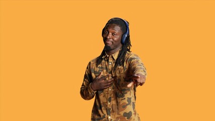 African american guy enjoying music on headphones, having fun with groovy dance moves in studio. Young joyful person listening to his songs on audio headset, dancing on camera.