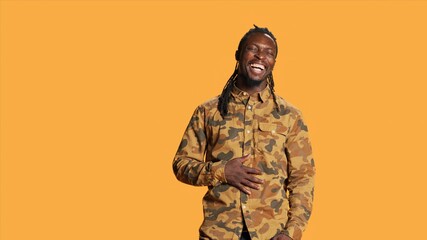Cheerful adult enjoying shoot and laughing on camera, making jokes in studio and acting playful. Silly positive african american guy having fun over orange background, relaxed casual person.