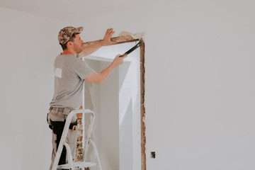 A young Caucasian male builder clears a doorway using a crowbar.