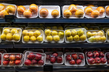 Packaged apples and oranges on the supermarket shelf.