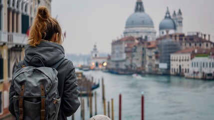 Fototapeta na wymiar Woman traveler with backpack looking at Grand Canal and Basilica Santa Maria della Salute in Venice, Italy