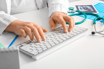 Female doctor working with computer keyboard on white medical desk, closeup