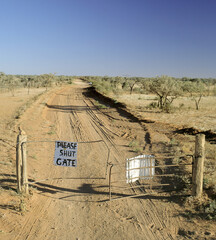 Dirt track in outback Queensland with please shut gate sign for passing travellers.