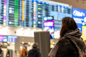 View from the back of a female tourist standing at the airport and looking at the dashboard that...