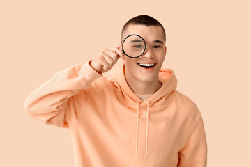 Young man with magnifier on beige background