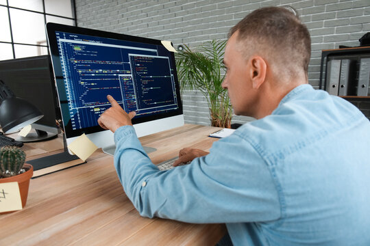 Mature male programmer pointing at computer monitor with programming code in office