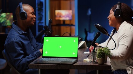 Green screen laptop next to man on podcast discussing with guest during marathon stream for...