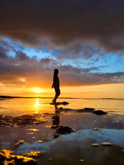 a modest silhouette of a young, sweet girl, a modest, charming woman at a golden sunset, against the backdrop of a dark blue sky with blue sparkles. The silhouette is reflected in the sea water, like 