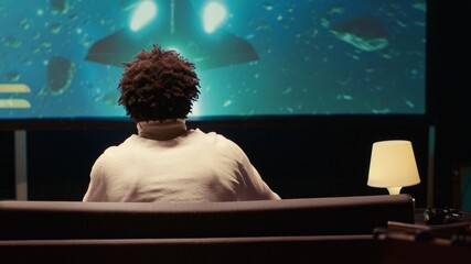 Man plays singleplayer game with spaceship shooting laser streams at asteroid, using crosshair overlay to hit targets and win mission. Ray tracing graphics and high FPS scifi videogame displayed on TV