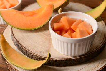 Board and bowl with pieces of sweet melon on wooden table