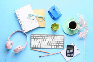 Composition with modern computer keyboard, headphones, cup of coffee and stationery on blue background