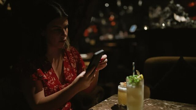 Beautiful hispanic woman in glasses captures a fun moment, snapping a picture of her tropical cocktail drink at a lively club