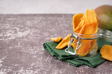 Jar with slices of dried mango on dark table