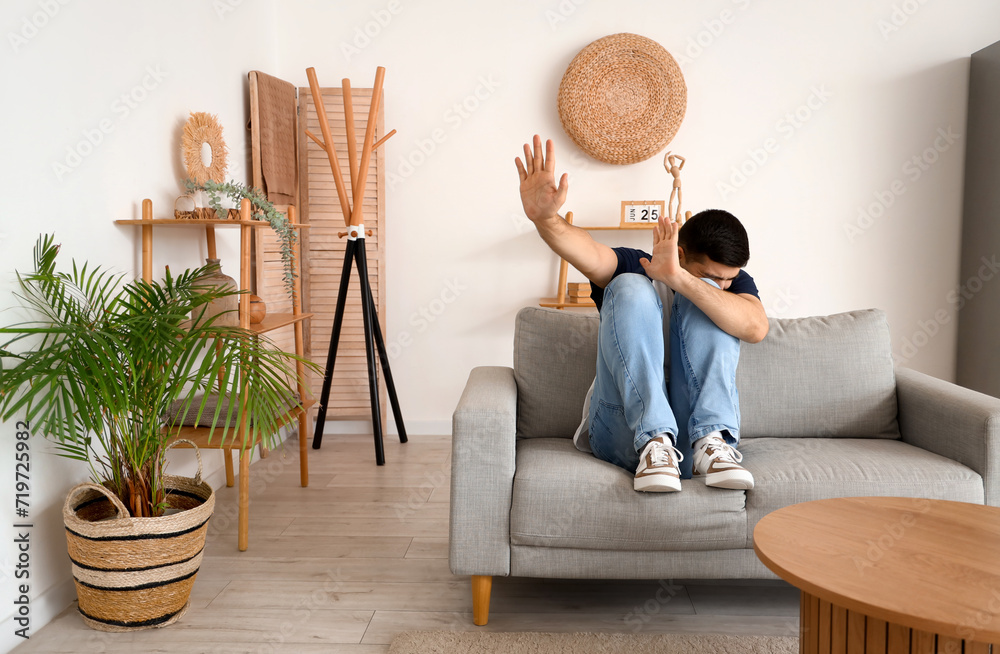 Wall mural afraid young man sitting on sofa in living room