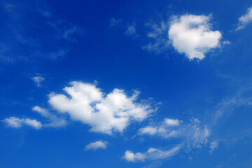 two white fair weather clouds, cumulus in the blue sky