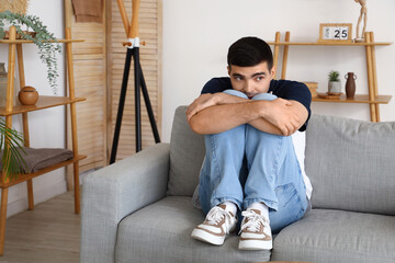 Afraid young man sitting on sofa in living room