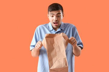 Afraid young man with shopping bag on orange background