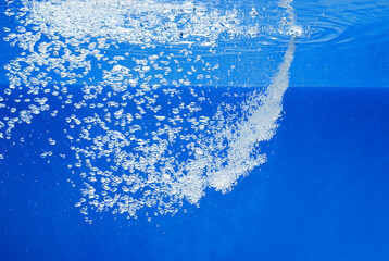 a thin jet of water penetrates the water surface and produces many air bubbles in the blue water of...